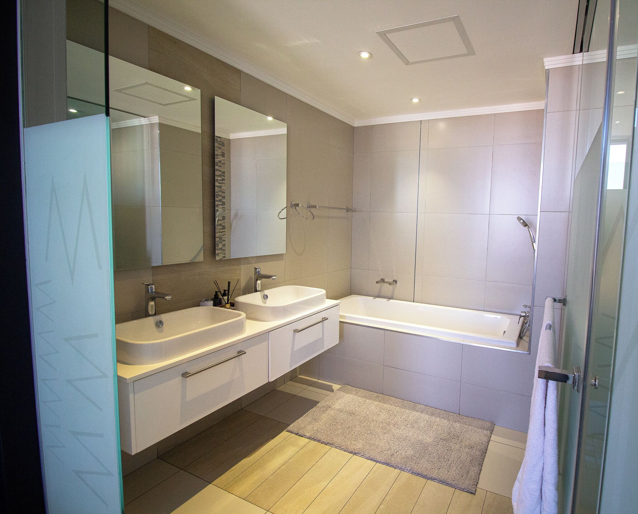 Een moderne badkamer met twee wastafels, een grote spiegel, een douche en een glazen deur.