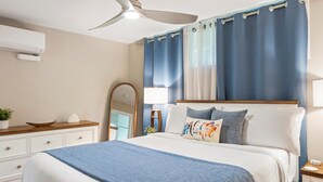 A bedroom with a bed, a ceiling fan, a mirror, a nightstand, and a window with curtains. - Summer Deal Ground Floor Kihei Condo Walk to Beach and Surf Spots (Kihei)