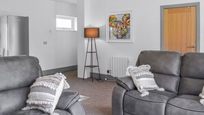 A modern living room with two grey leather sofas, a floor lamp, a radiator, and a colorful abstract painting on the wall. - Emmotland Retreat - UK44180 (Driffield)
