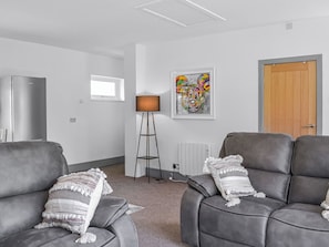 Een moderne woonkamer met twee grijze leren banken, een vloerlamp, een radiator en een kleurrijk abstract schilderij aan de muur.