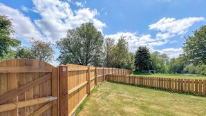 A wooden fence with a gate, a paved walkway, and a grassy yard with trees in the background. - Emmotland Retreat - UK44180 (Driffield)