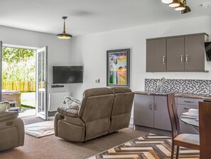 Una sala de estar moderna con un sofá, un televisor y una zona de cocina con armarios y un salpicadero de azulejos.