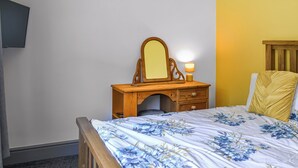A bedroom with a wooden dresser, a mirror, a bedside lamp, and a bed with floral bedding. - Emmotland Retreat - UK44180 (Driffield)
