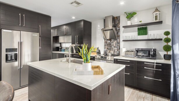Una cocina moderna con armarios oscuros, electrodomésticos de acero inoxidable, una isla central y plantas decorativas.