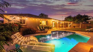 Una piscina con agua cristalina, rodeada de sillones de descanso y una terraza bien iluminada.