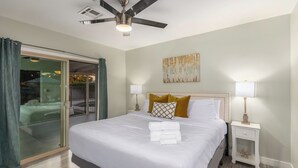 Habitación de hotel con una cama, dos lámparas de noche, un ventilador de techo, un cuadro en la pared y una puerta de vidrio que da a un espacio al aire libre.
