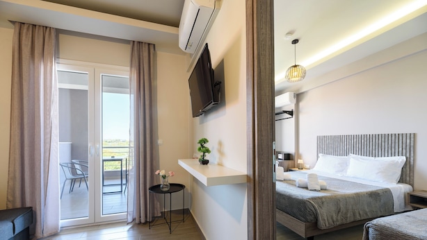 A hotel room with a bed, a TV, a small table with a plant, and a balcony with a chair. - Philippos Residences (Dio-Olympos)