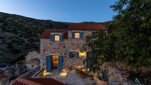Une maison en pierre avec un toit recouvert de tuiles rouges, un escalier en pierre et un espace extérieur aménagé avec des coussins.