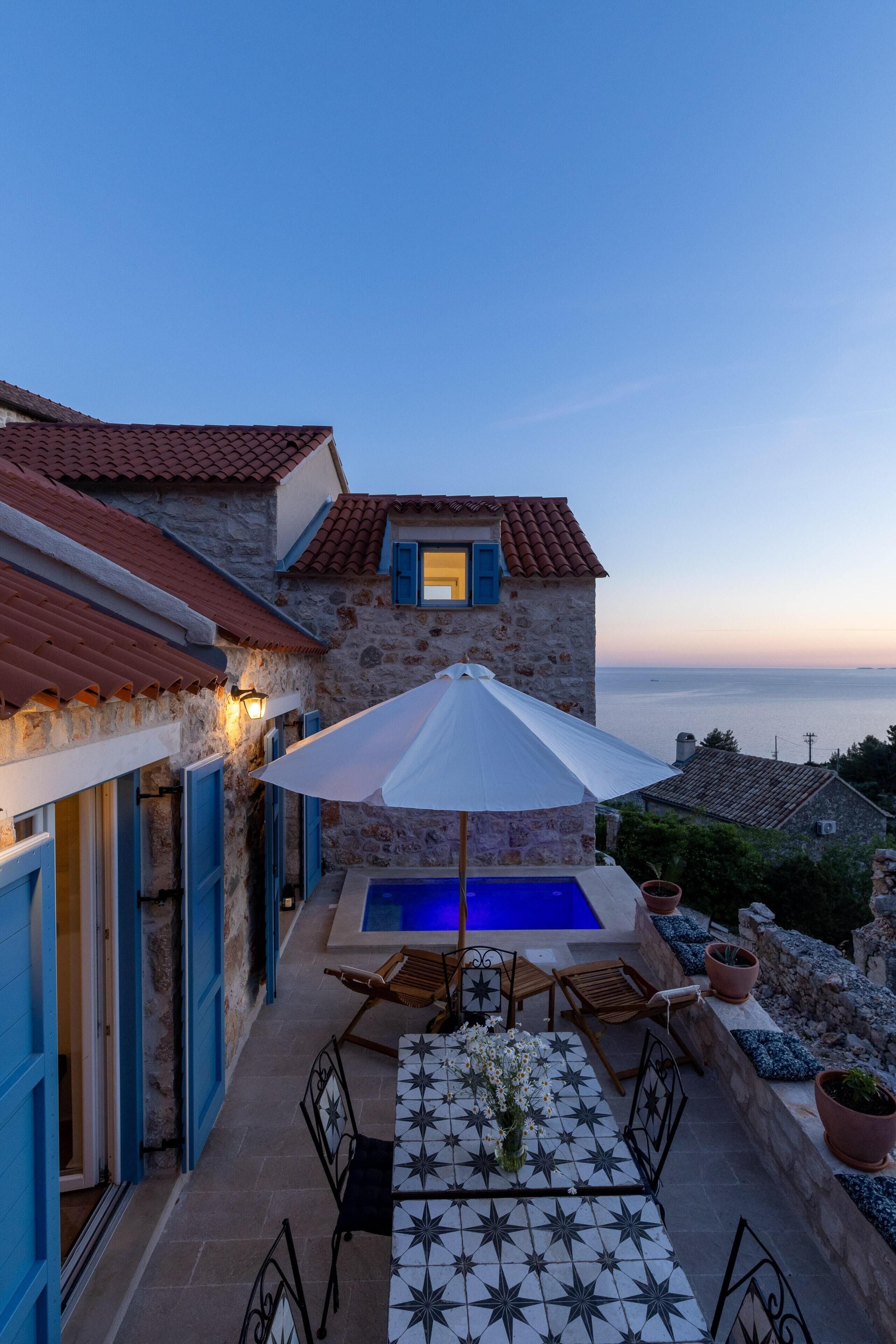 A stone building with a pool, outdoor seating, and a view of the sea.