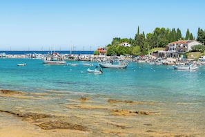 Uma marina costeira com barcos atracados, águas turquesa cristalinas e edifícios com telhados vermelhos.