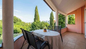 A covered outdoor area with a table and chairs, a view of trees and buildings, and a tiled floor. - Holiday apartment with air conditioning and internet (Umag)