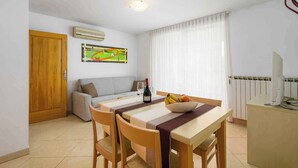 A dining area with a table, chairs, a bowl of fruit, a bottle of wine, and a painting on the wall. - Holiday apartment with air conditioning and internet (Umag)