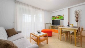 A living room with a sofa, a coffee table, a dining table with chairs, a television, and a decorative vase. - Holiday apartment with air conditioning and internet (Umag)
