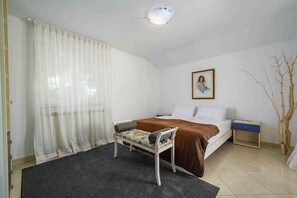 Um quarto com cama, mesa de cabeceira, cadeira, quadro na parede e janela com cortinas.