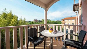A balcony with a round table and two chairs, a vase with flowers, and a view of buildings and trees. - Holiday flat with air conditioning and internet (Umag)