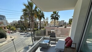 Ein Balkon mit Glasgeländer, einem kleinen Tisch, zwei Stühlen und einem roten Kissen.