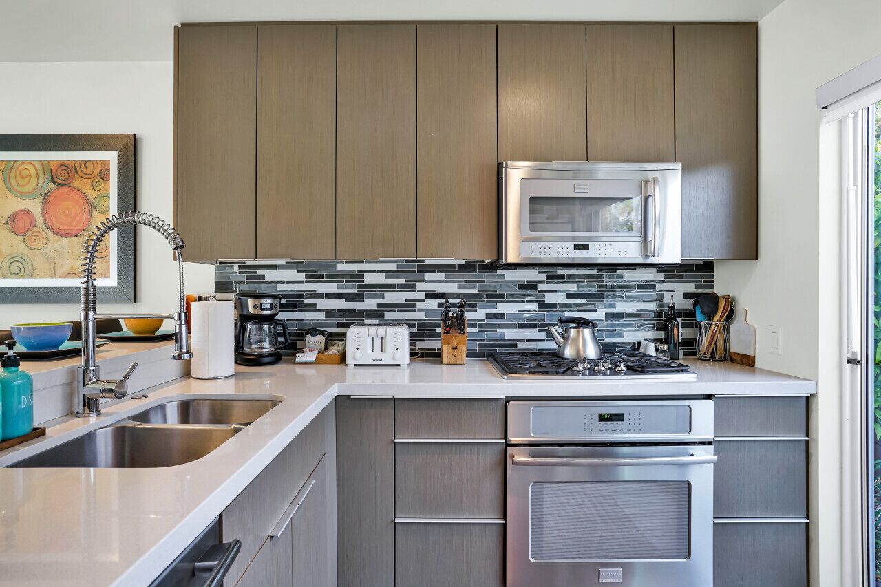 A modern kitchen with stainless steel appliances, a tiled backsplash, and wooden cabinets.