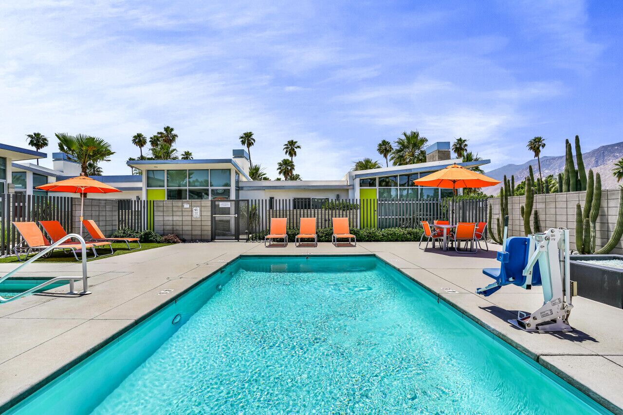 A pool area with a rectangular pool, orange lounge chairs, and umbrellas.