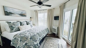 Quarto com cama, ventoinha no teto, janela com cortinas, televisão e um quadro na parede.