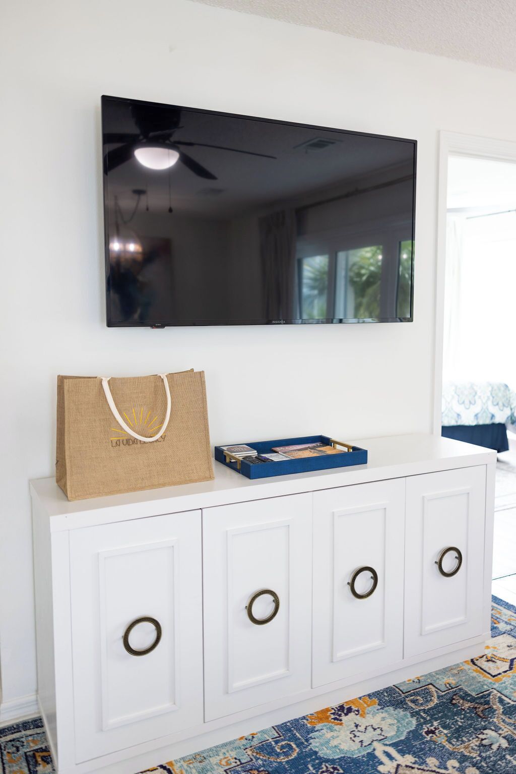 A white cabinet with circular handles, a television mounted above it, and a blue tray with books and a brown paper bag on top.