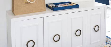 A white cabinet with circular handles, a television mounted above it, and a blue tray with books and a brown paper bag on top.