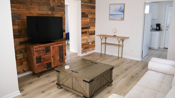 Una sala de estar con pared de madera, un televisor sobre un mueble, una mesa de centro y un sofá.