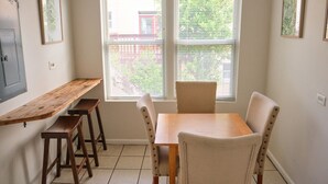 Un comedor con una mesa de madera y cuatro sillas, una ventana con persianas y dos cuadros en la pared.