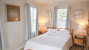 Un dormitorio con una cama de madera, dos mesitas de noche y un ventanal con cortinas.