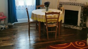 Un coin repas avec une table dressée pour deux personnes, une chaise, un vase avec des fleurs, une cheminée et une horloge murale.