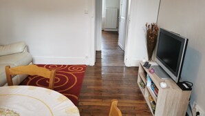 Une petite pièce agréable et chaleureuse, avec un lit, une chaise en bois, un téléviseur posé sur un meuble en bois et une bibliothèque.