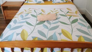 Un lit avec une couvre-lit à motifs de feuilles, une tête de lit en bois et une table de chevet en bois dotée d’un tiroir.