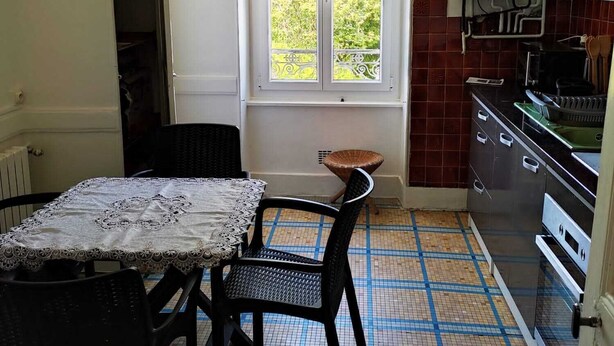 Une cuisine compacte avec un coin repas, une fenêtre donnant sur un espace verdoyant et un revêtement de sol carrelé.