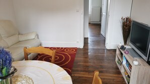 Un salon avec un canapé, une chaise en bois, un téléviseur posé sur un meuble en bois et une bibliothèque.