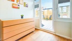 Ett rum med en byrå i trä, en krukväxt och en skjutdörr i glas som leder ut till en uteplats med ett bord och stolar.