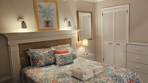 Een slaapkamer met een bed, nachtkastje, dressoir, spiegel en een wandlamp.