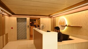 Un hall d’hôtel avec un comptoir d’accueil en bois, un ventilateur et une enseigne sur laquelle on peut lire « Hadi ».