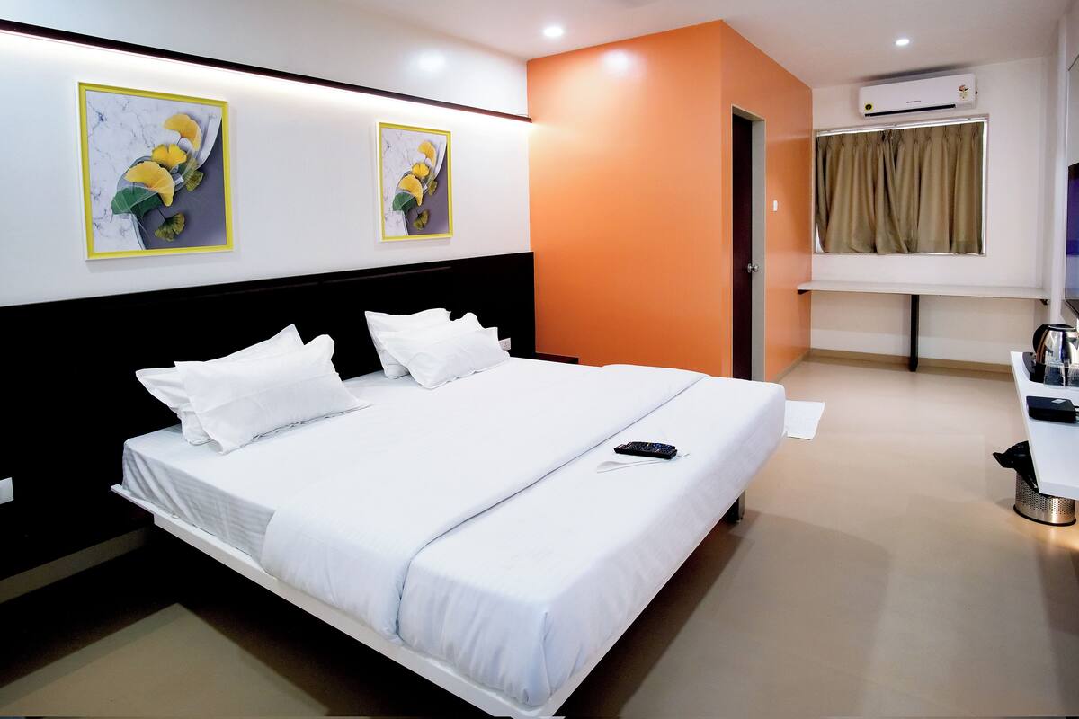 Quarto de hotel com uma cama grande, uma mesa com cadeira, aparelho de ar condicionado e duas obras de arte emolduradas na parede.