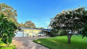 Una casa con entrada pavimentada que conduce a un garaje, rodeada de follaje y árboles.