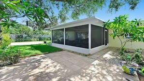 Una casa moderna con un patio cubierto, rodeada de abundante vegetación y un césped cuidado.