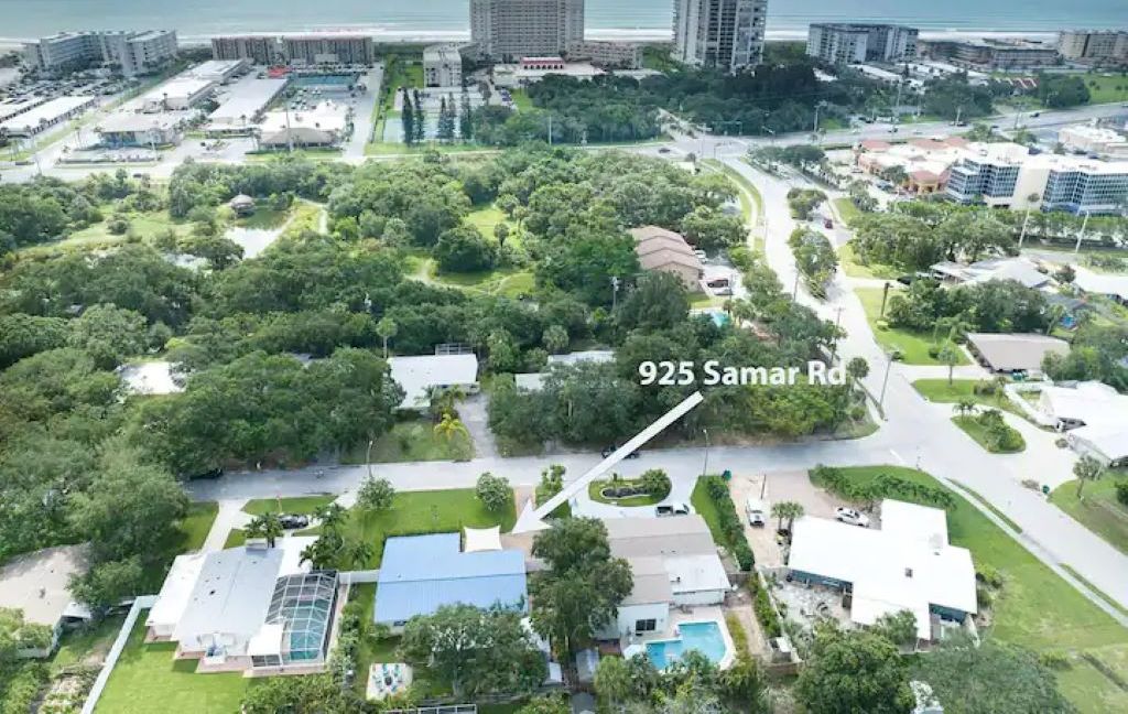 An aerial view of a coastal area with dense greenery, a road labeled '925 Samar Rd', and buildings in the background.