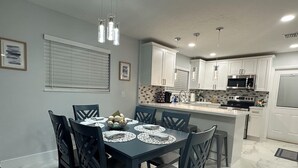 A modern kitchen with white cabinets, a central island, and a dining area with a table set for six. - Home Away From Home! (Vero Beach)