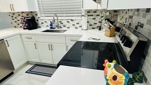 A modern kitchen with white cabinets, a black stove, and a decorative ceramic frog on the counter. - Home Away From Home! (Vero Beach)