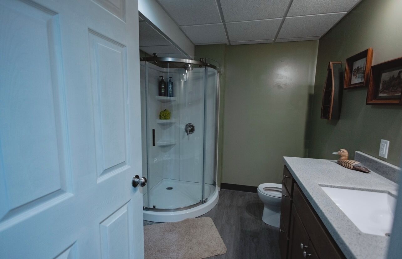 A bathroom with a glass shower enclosure, a toilet, a sink with a towel, and framed pictures on the wall.