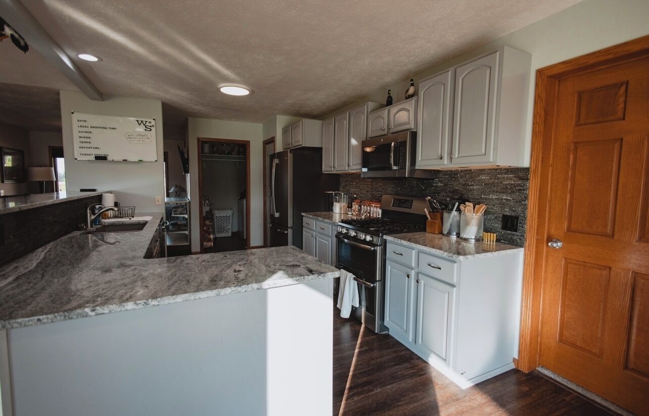 A kitchen with white cabinets, a black refrigerator, a stove, and a microwave. There is a wooden door on the right and a whiteboard on the wall.