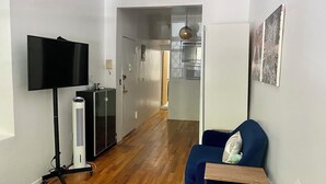 Una sala de estar con un televisor de pantalla plana, un calefactor, un sofá azul y una cocina al fondo.