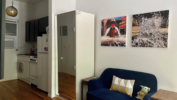 Un espacio habitable compacto con kitchenette, un sofá azul con un cojín mullido y dos cuadros enmarcados en la pared.