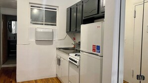 Una cocina compacta con ventana, un refrigerador, una estufa y armarios oscuros.