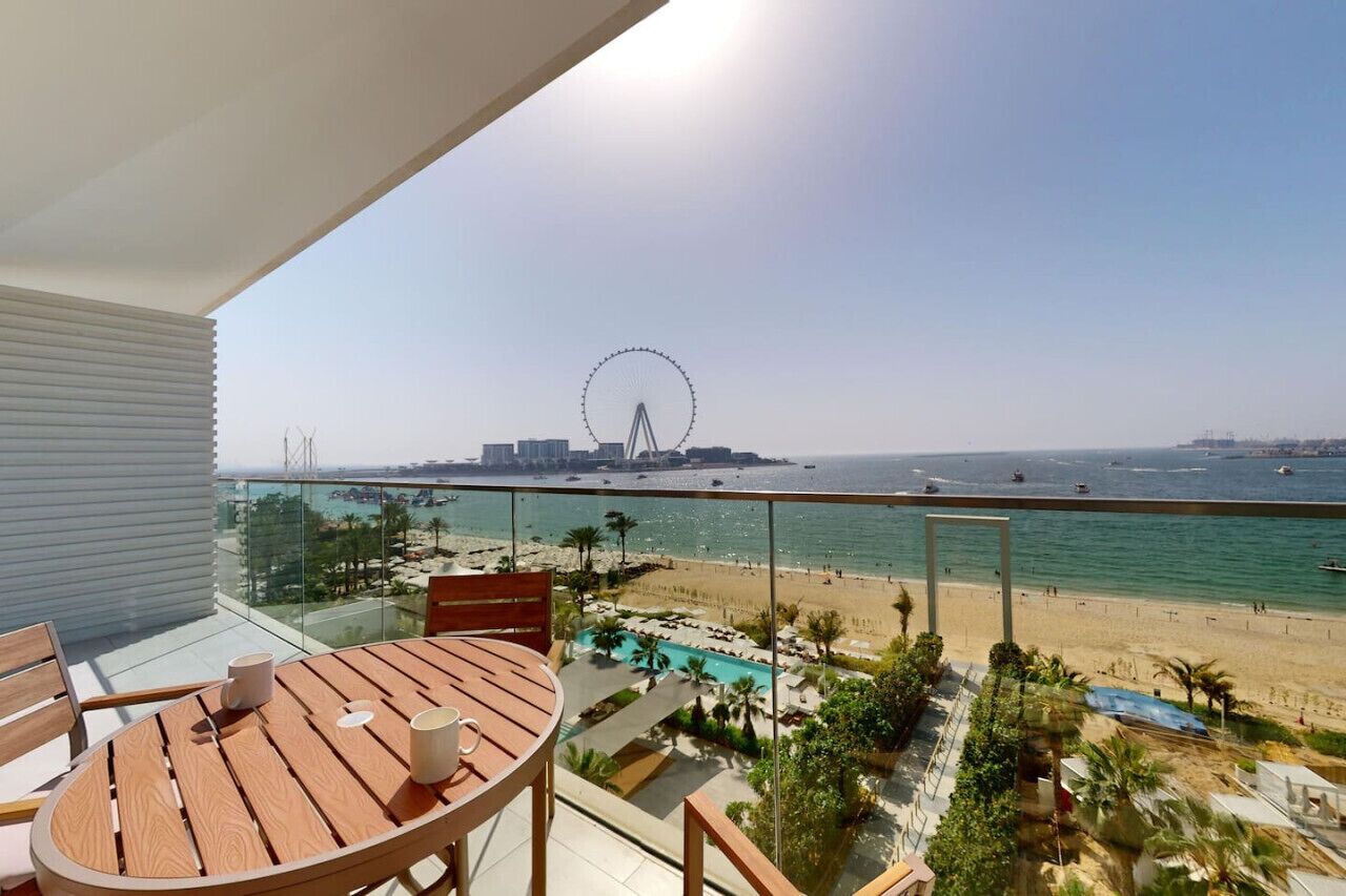 Ein Balkon mit Holztisch und Stühlen, der auf einen Strand mit einem Riesenrad im Hintergrund blickt.