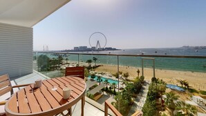 Ein Balkon mit Holztisch und Stühlen, der auf einen Strand mit einem Riesenrad im Hintergrund blickt.