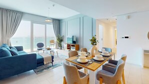 Ein modernes Wohnzimmer mit einem blauen Sofa, einem Esstisch für vier Personen und einem Fernseher im Hintergrund.